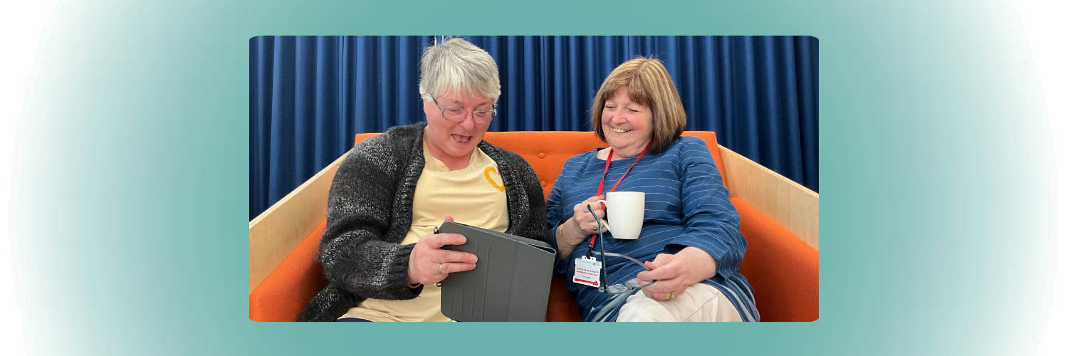 Two people on an orange sofa drinking coffee and looking at an iPad