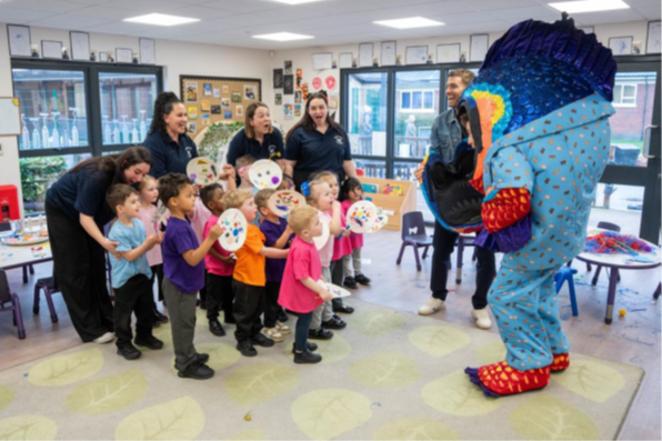 A group of young children, attentively watching a person in a colourful, large fish costume