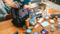 A person packing a backpack with various travel items