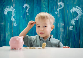 A child sitting at a table with a piggy bank and coins