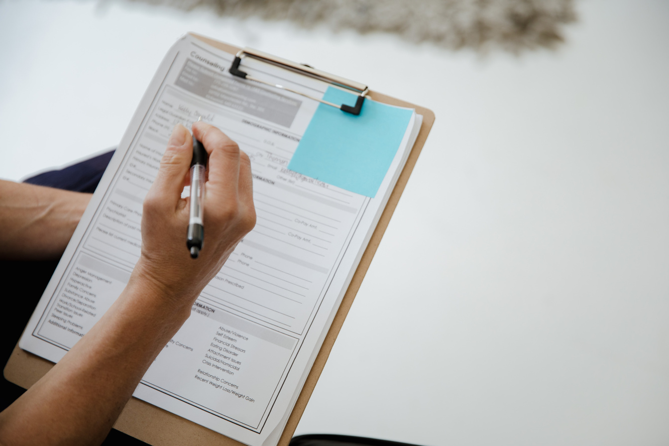 A person filling out a form on a clipboard with a pen