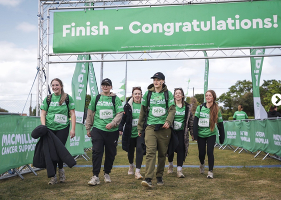 A group of six people walking under a green "Finish – Congratulations!" banner at a Macmillan Cancer Support event.