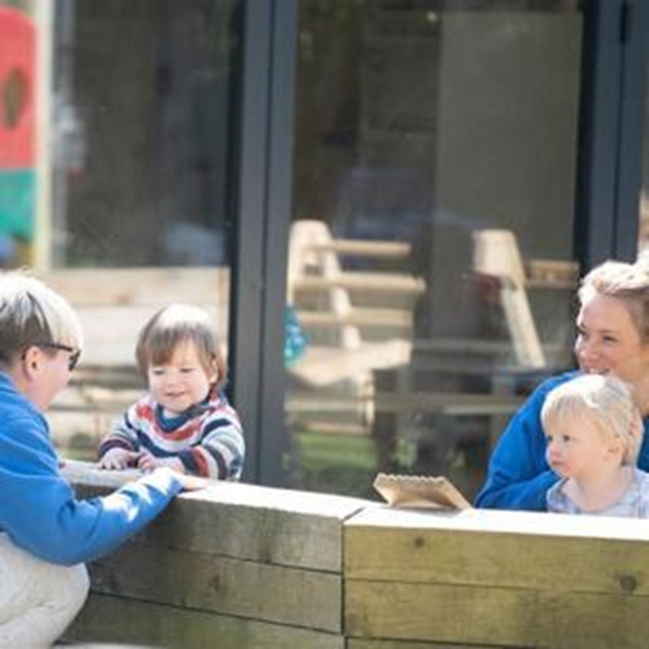 Two adults and children sitting along a wooden wall