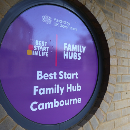 Photograph showing a circular purple sign identifying Best Start Family Hub Cambourne, funded by UK Government.