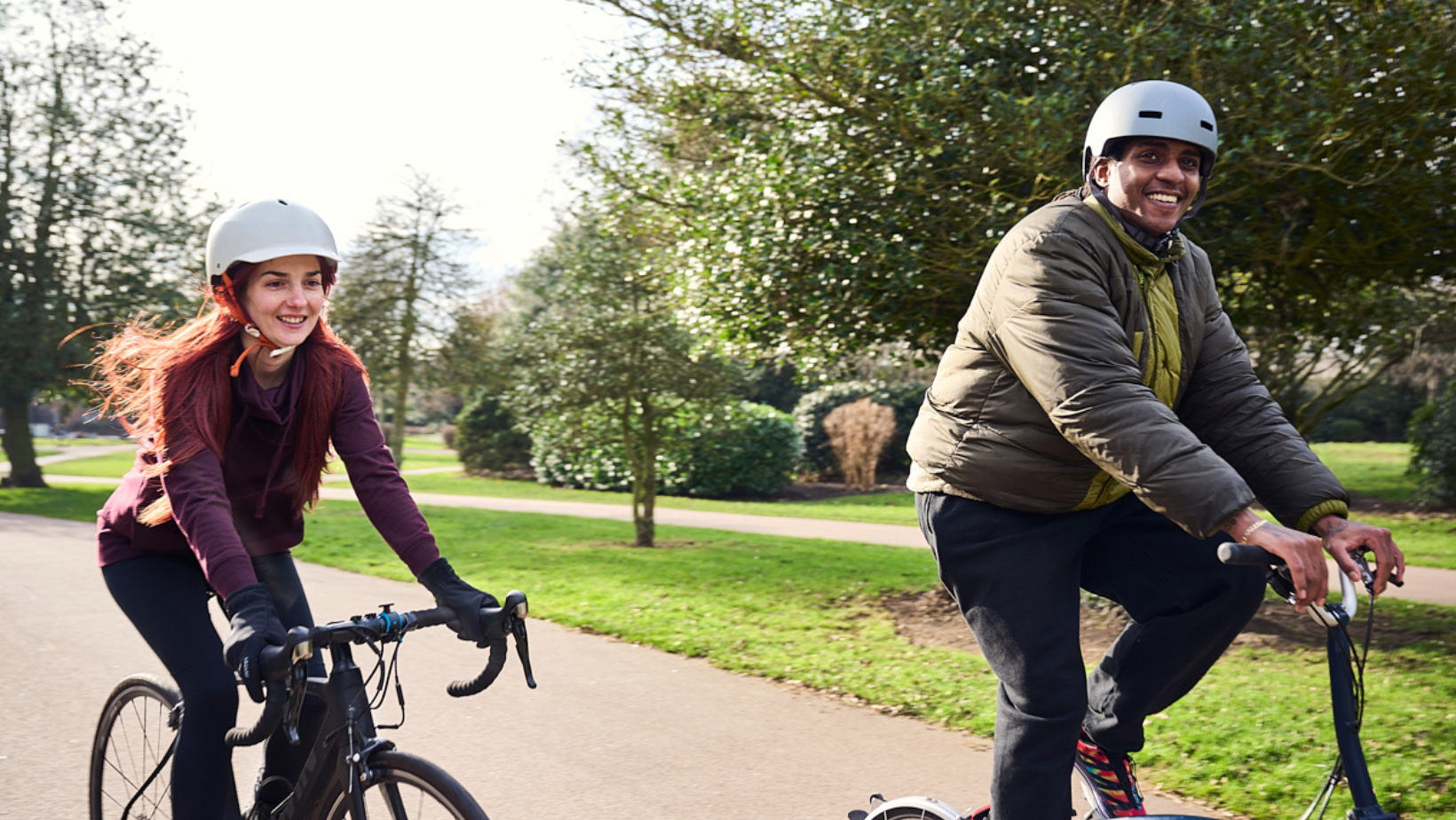Two people smiling and riding bikes in the park