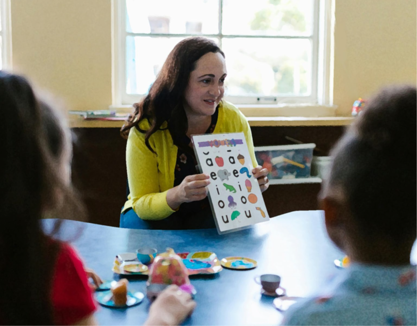 Adult showing letters on a A4 sheet of paper to infant children