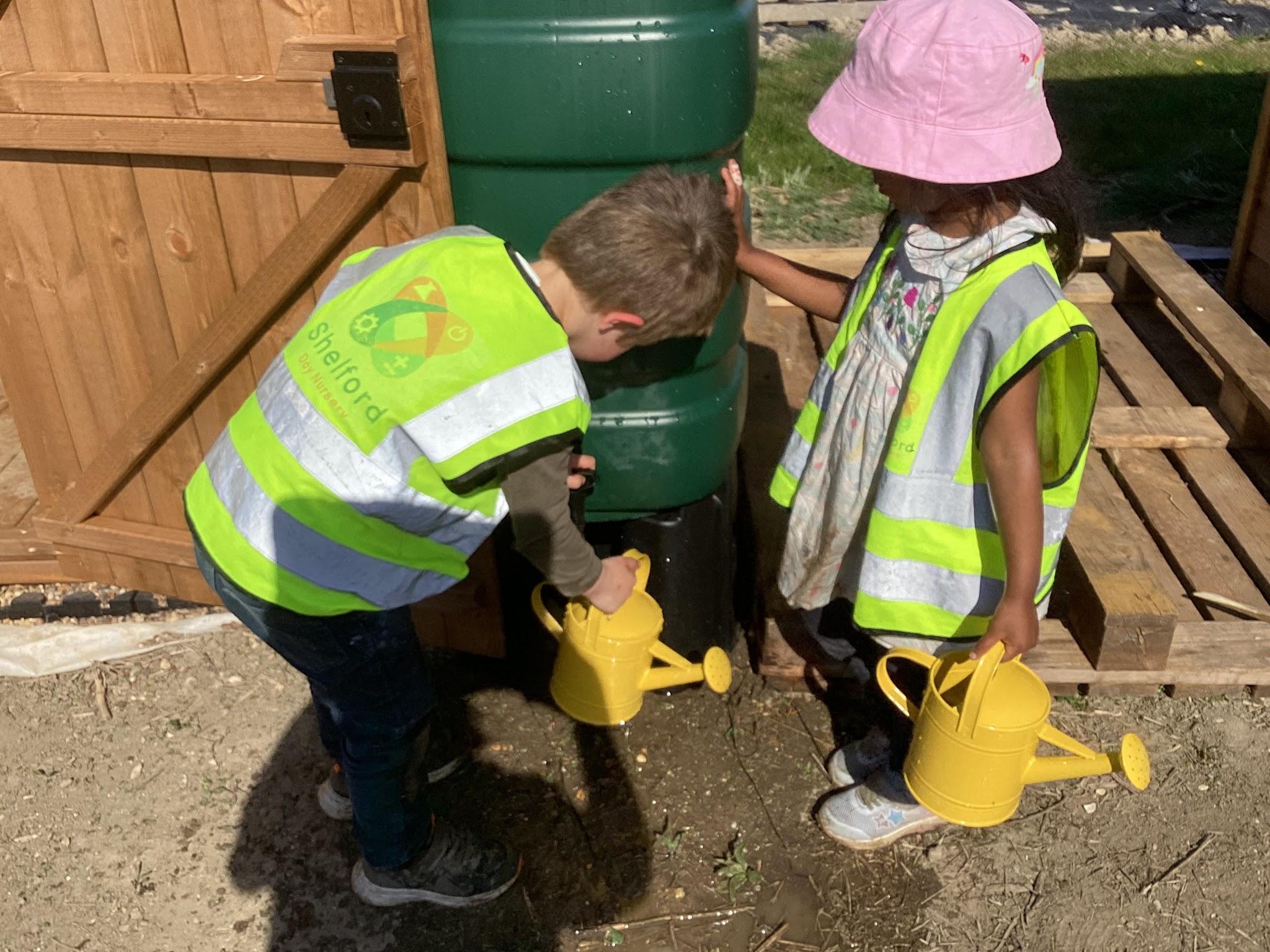 A couple of young children wearing safety vests filling up watering cans