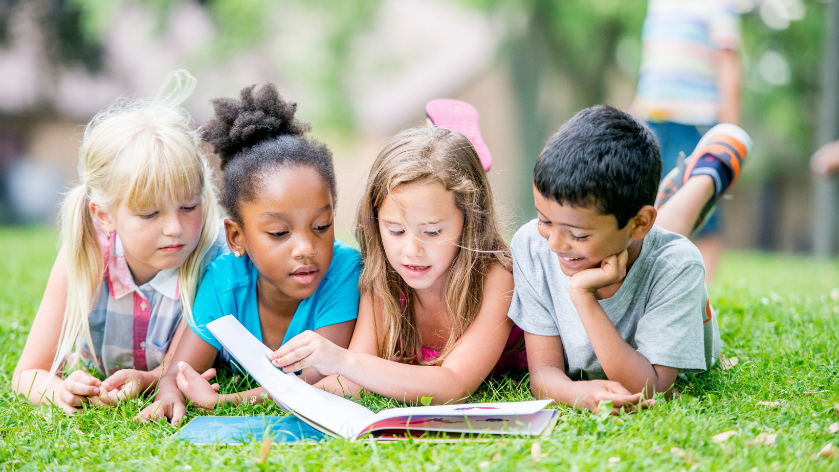 Group of four children reading a book on the grass