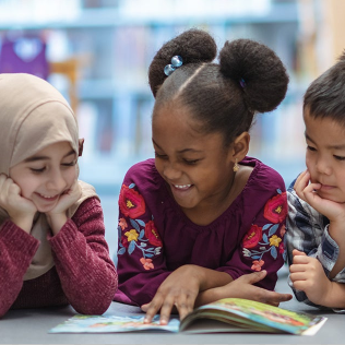 A group of children reading a book on the floor