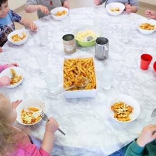 A group of children sitting around a table, eating pasta from bowls