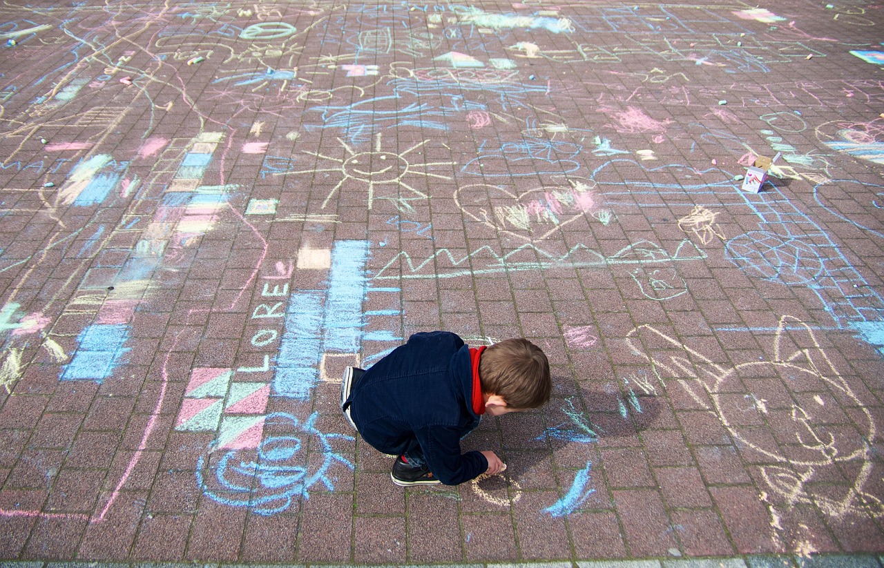 Child creating colourful chalk drawings on a paved surface filled with playful designs