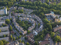 Aerial view of an urban estate, with a semi-circle of low-rise properties surrounded by trees and tower blocks.
