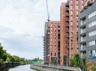 A row of recently built apartment blocks overlooking a canal, with a builder's crane in the background.