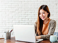 A laptop user looks at her screen while typing, with a coffee cup and a bucket of pens on either side of her desk.