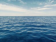 An empty stretch of sea, slightly ruffled by the wind and stretching away to the horizon, with patchy white clouds above.