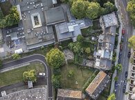 An aerial view of a diverse collection of neighbouring buildings, some facing onto a road on the right and some set back from the road.