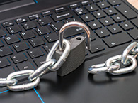 An open padlock sitting on a laptop keyboard, with a chain linked to the padlock on the left but the other end lying flat to the right.