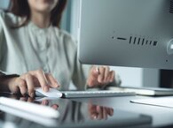 An office worker uses a desktop computer mouse with her right hand while looking at the computer screen.