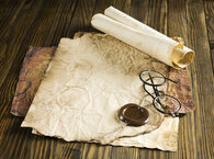 An ageing document with a seal lying flat on a desk, with spectacles and a scroll lying on it.