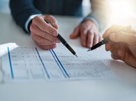 Two people examine a document with pens in hand.