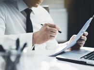 A conveyancer in shirt and tie working at a desk, with a document in one hand and a pen in the other.