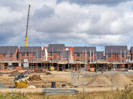 A construction site with a crane and a row of homes in the background.
