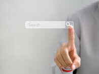 A figure behind a screen points with their right hand to a search icon on the screen.