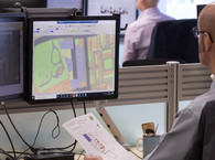 An HM Land Registry caseworker examines a plan on a desktop screen, while holding a paper document in their left hand.