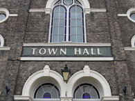 The facade above the entrance to a Victorian town hall, with the words 'Town Hall' emblazoned above and below medieval-style windows.