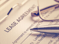 The head of a pen and a frame of a pair of spectacles lying on a document on a clipboard titled 'Lease agreement'.