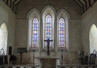 A church altar topped by a large crucifix and with a three-bay stained glass window behind,