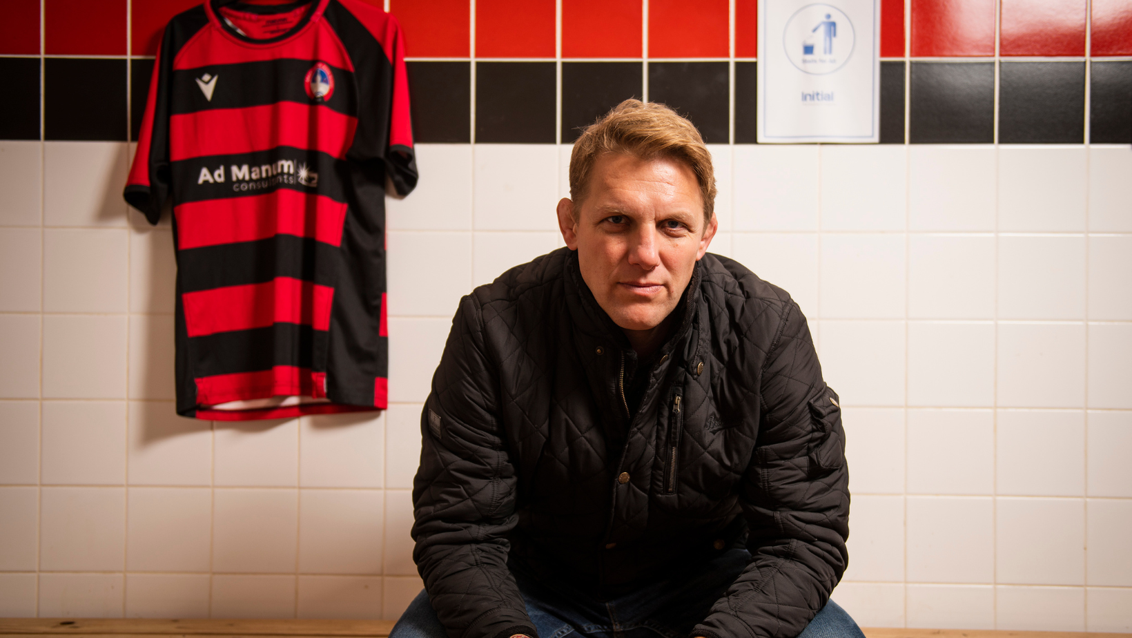 An image of Lewis Moody MBE for the Stalls For All campaign sat on a bench with a rugby t-shirt in the background